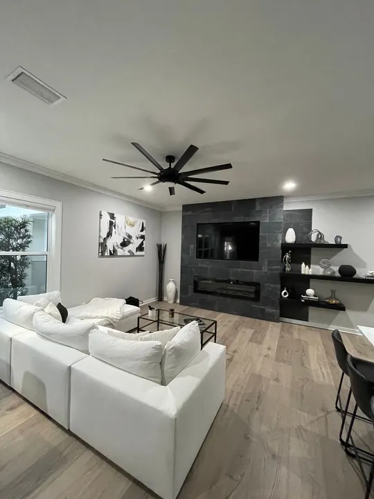 Living room entertainment wall with a built-in TV above a linear fireplace in dark tile, with floating shelves